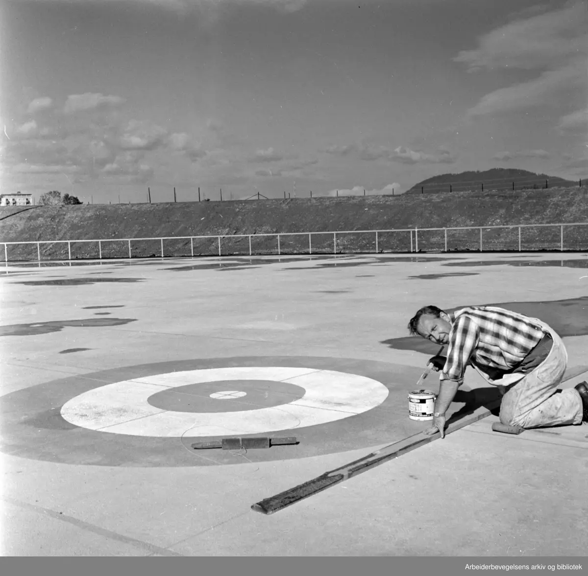 Valle- Hovin: Mange slag idretter vil få plass på den nye banen. Curling er en av dem, og her er Håkon Kristiansen i full gang med å gi betongdekket de rette merkene. September 1966
