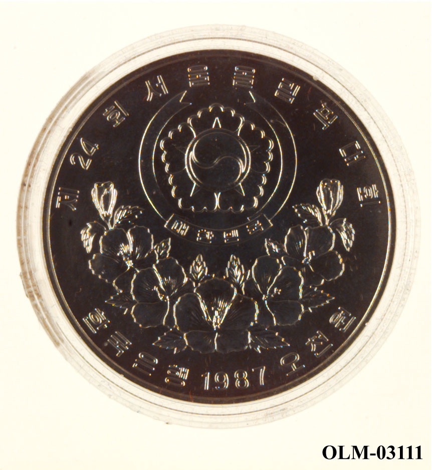 Mynt som viser to barn p den ene siden og og seks lotusblomster under jing yng symbol på den andre siden. Mynten ligger i en sølvfarget eske merket Seoul 1988.