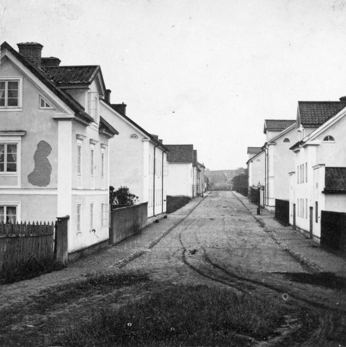 Suddig men unik vy från Linköping. Drottninggatan sedd västerut från Magasintorget. Avsaknaden av senare, känd förändring av miljön daterar bilden till före 1869. Fototiden uppskattad till omkring 1865.