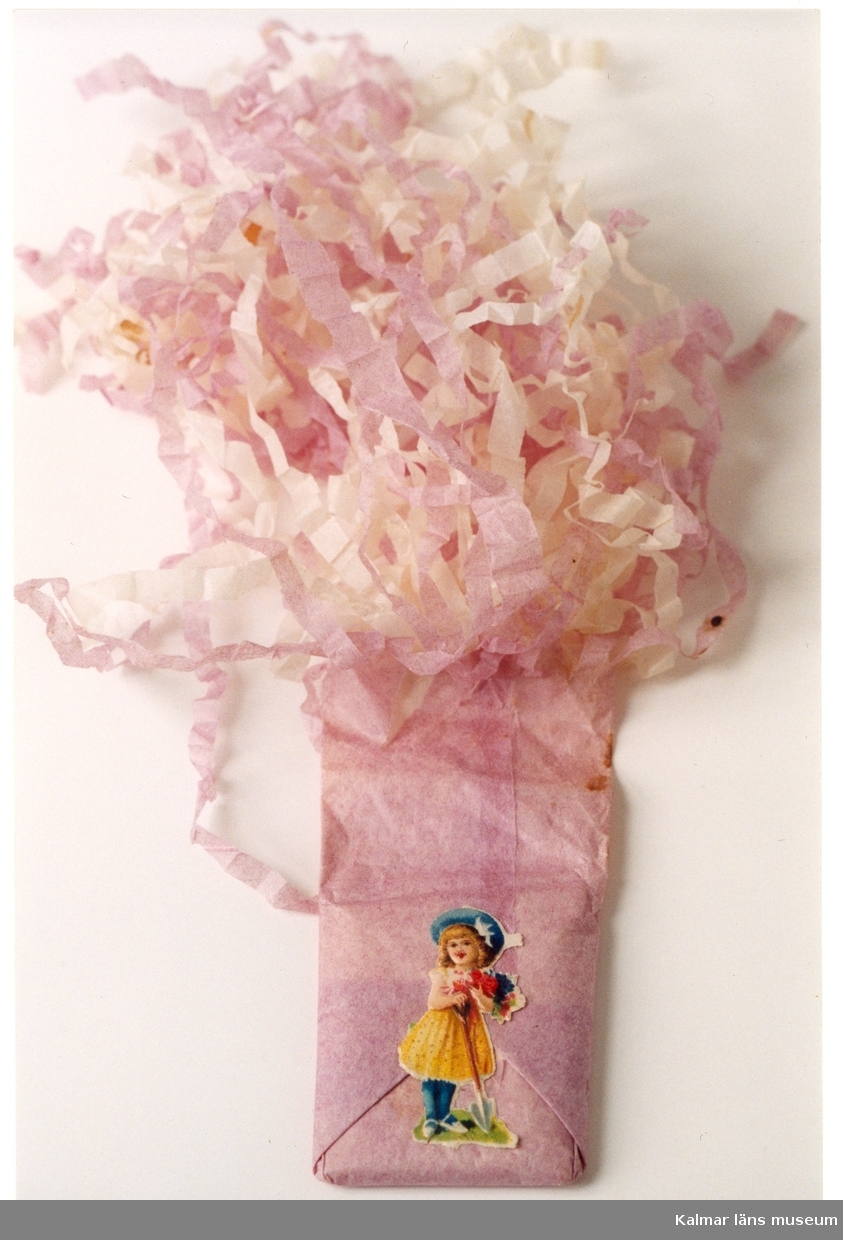 KLM 31514:4. Julgranskaramell, av silkespapper, med konfekt. Av lila och vitt papper, med bokmärke, motiv med flicka i bredbrettad hatt, spade och blommor. På baksidan text, Fr. Johan till mormor.