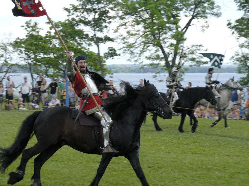 Middelalderridder som rir på svart hest, med middelalderfane i ene hånda.