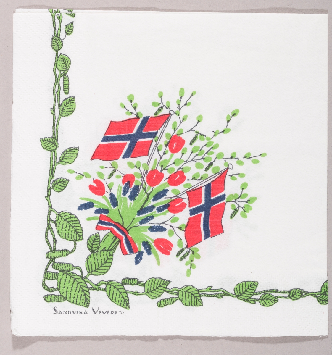 To norske flagg i en bukett med grønne bjørkegrener og røde og blå blomster. En bord med grønne blader og rakler.