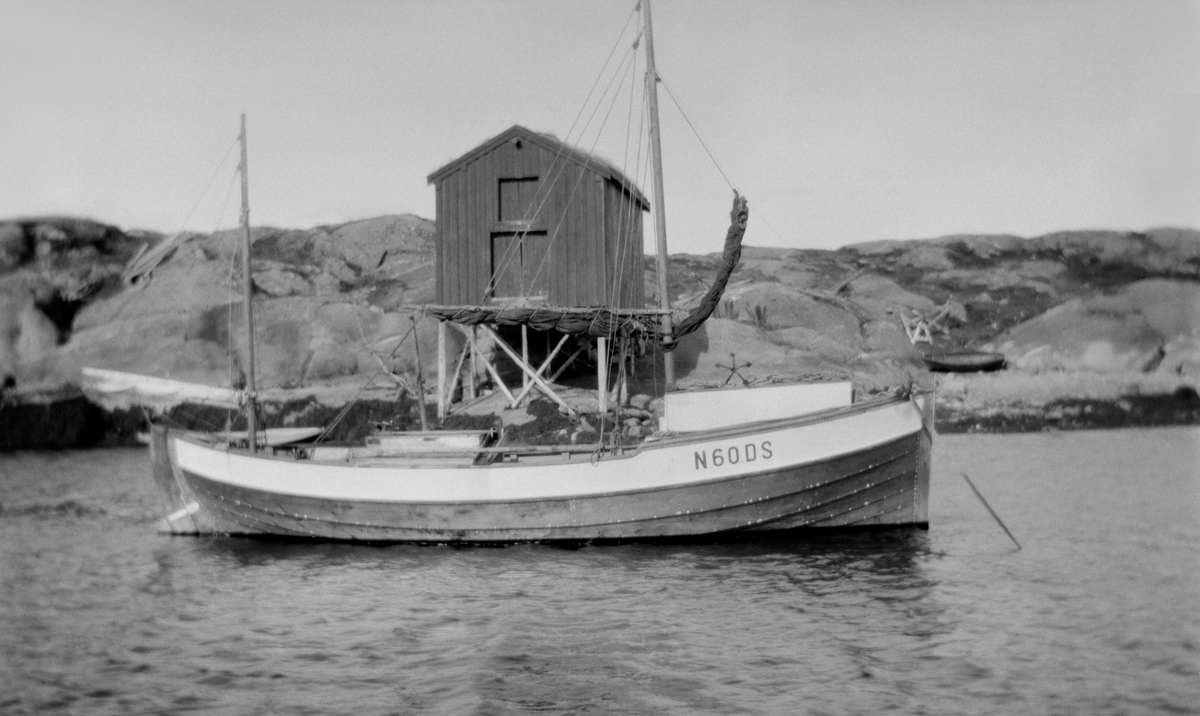Båt merket N-60-DS ved land med brygge i bakgrunnen.