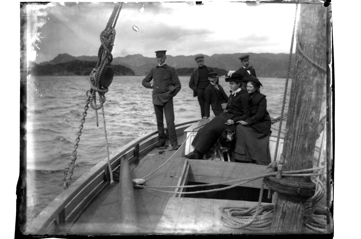 Fire menn og to kvinner ombord i seilbåt i ukjent farvann. Antagelig fotografert 1903-04.