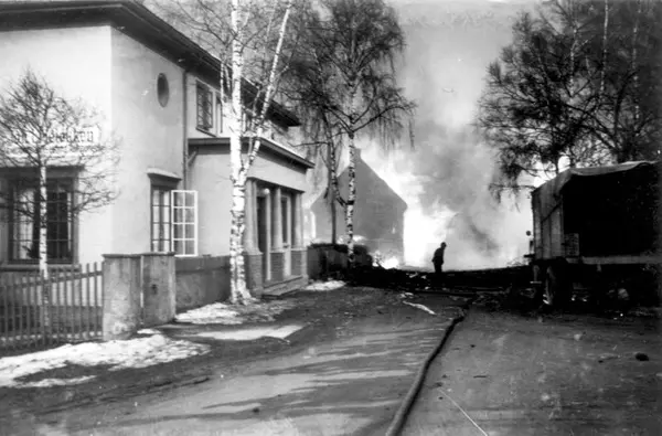 Et murbygg klarer seg gjennom bombingen. Brennende hus i bakgrunnen.