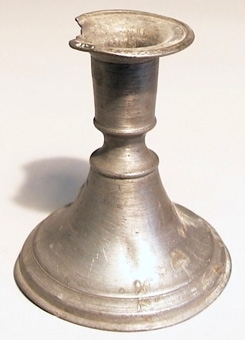 Ljusstake av tenn med klockformad fot och ett kort insvängt skaft. Ljusstaken har cylindrisk ljuspipa med en fast manschett.