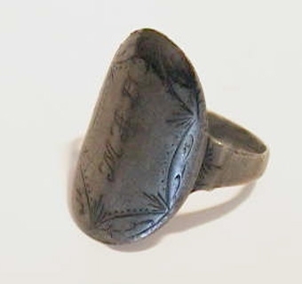 Fingerring av silver med kraftigt ovalformat framstycke. Framstycket är graverat för utsmyckning samt med initialer.