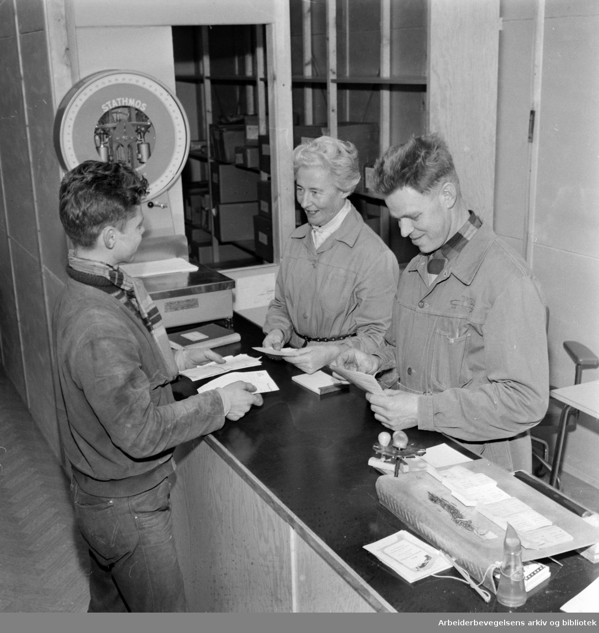 Økern. Godsrutestasjonen. Til venstre står Hans Kopperud fra Jessheim-ruta. Han blir ekspedert av Ingrid Steen og Gustav Eek. Mars 1960