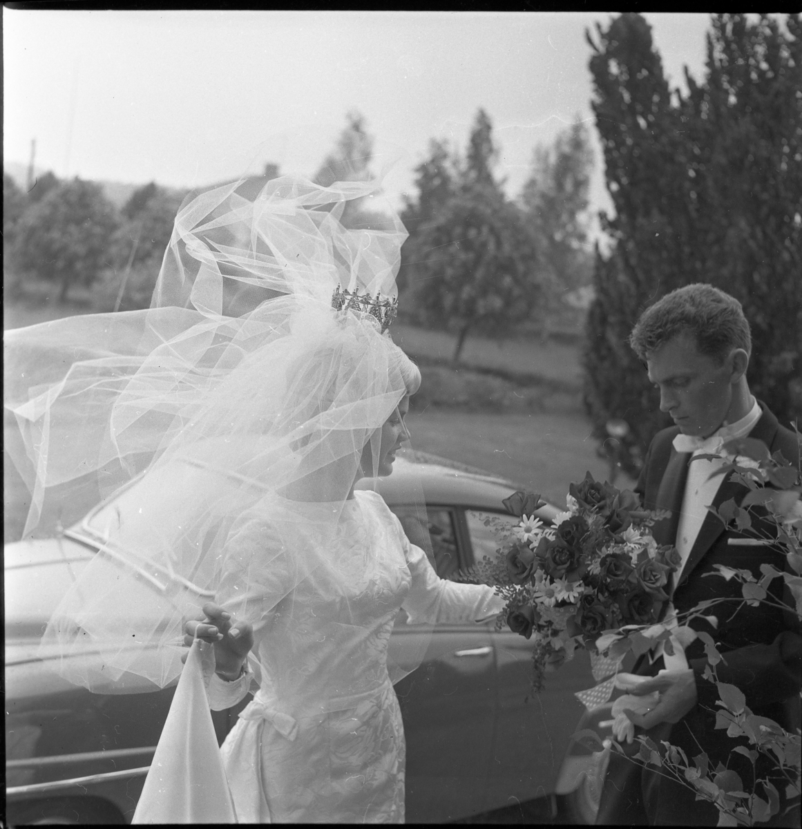 Nygifta Rolf Nilsson och Lisbeth Johansson utanför Örserums kyrka. Vinden sliter i brudslöjan. I bakgrunden står en SAAB.