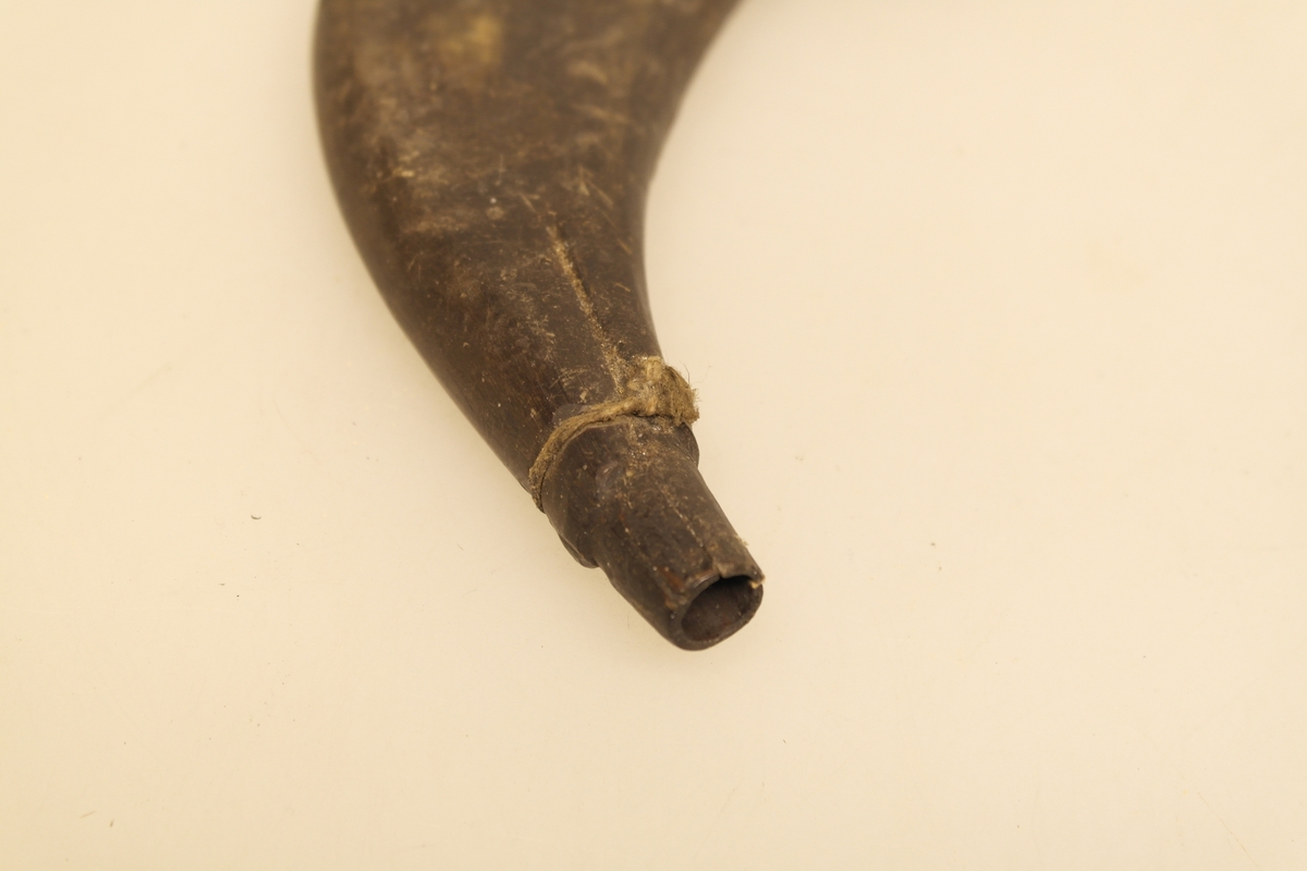 Krutthorn som er skåret og pusset. Den brede enden er trukket av en treplate. Det er rester av hyssing rundt åpningen. Geometrisk mønster (livets blomst) er risset inn på den ene siden av hornet. Brukt til oppbevaring av krutt.