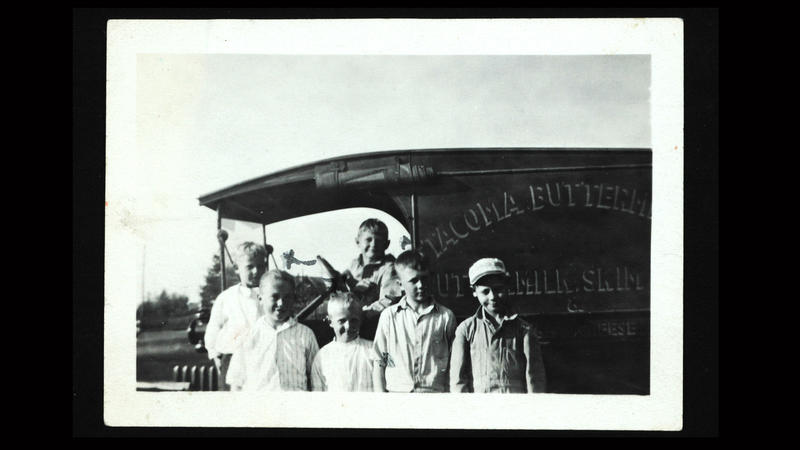 Seks barn avbildet med en eldre bil. Et barn i førersete og fem barn står foran. Bildet er ca. datert til starten av 1900-tallet.