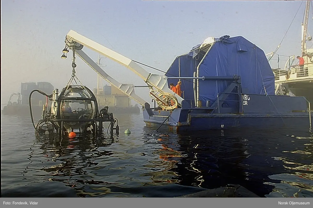 Miniubåten Check Mate fra "NUTEC" med to personer i er heises opp eller ned av vannet. Den henger i kranbommen på dykkerbåten "Strilborg", senere omdøpt til "Deepsea Inspector".