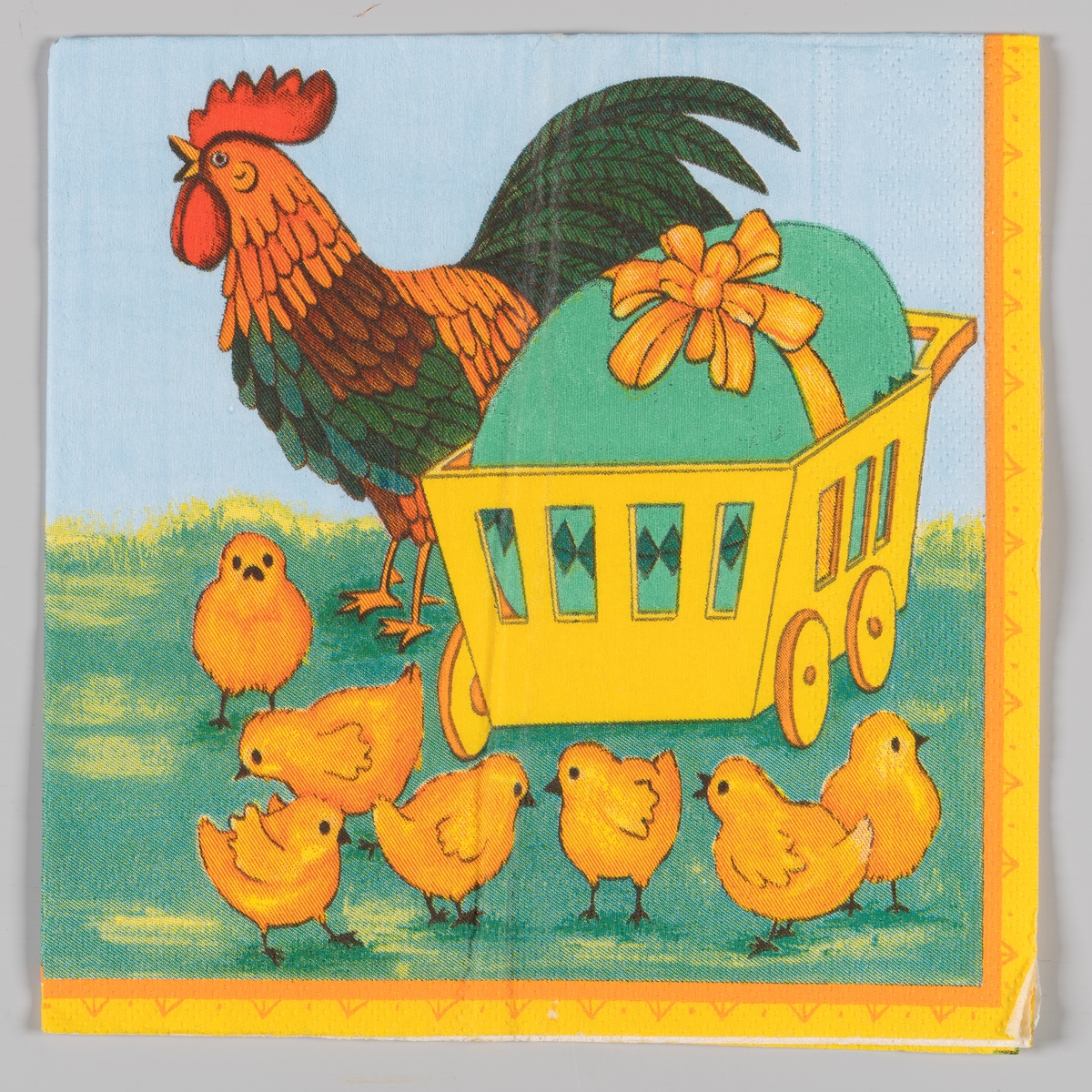 En trillevogn med et stort grønt påskeegg med sløyfe. En hane og en flokk med kyllinger.