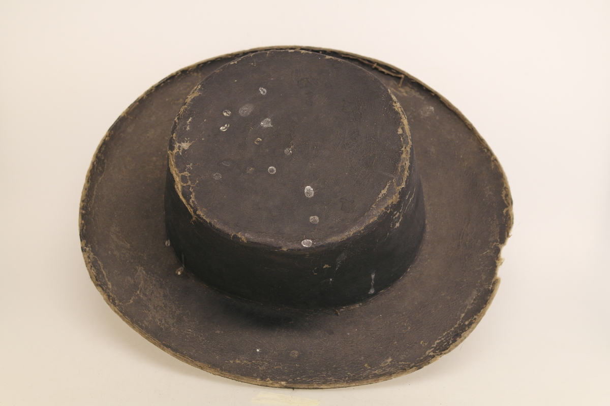 Svart filthatt med stiv pull og brem. Pullen er flat på toppen. Hatten er muligens malt svart.