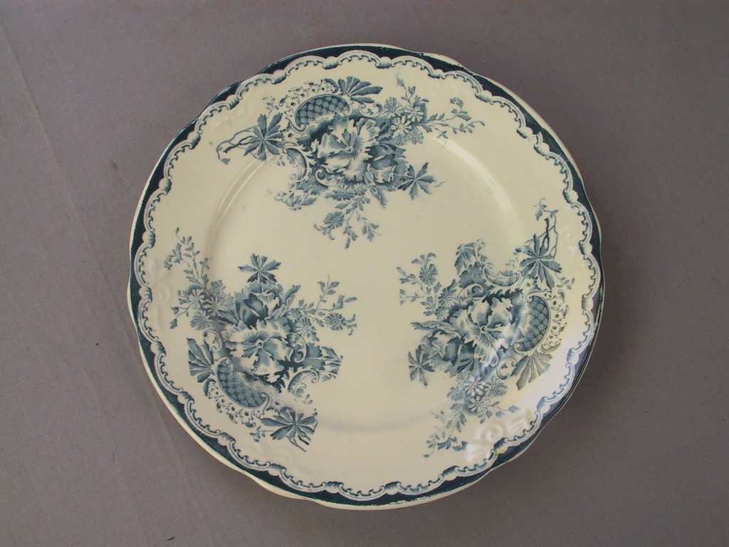 Sirkulært tverrsnitt

Bladornamentikk i relieff rundt kanten. Blå bord rundt kanten og 3 blomemotiv i same farge inni tallerken.

