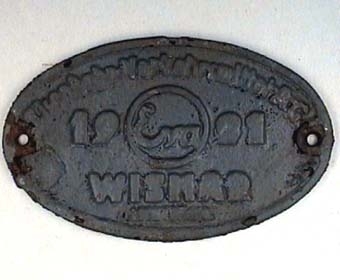 Oval skylt av grå gjutjärn med text i relief.