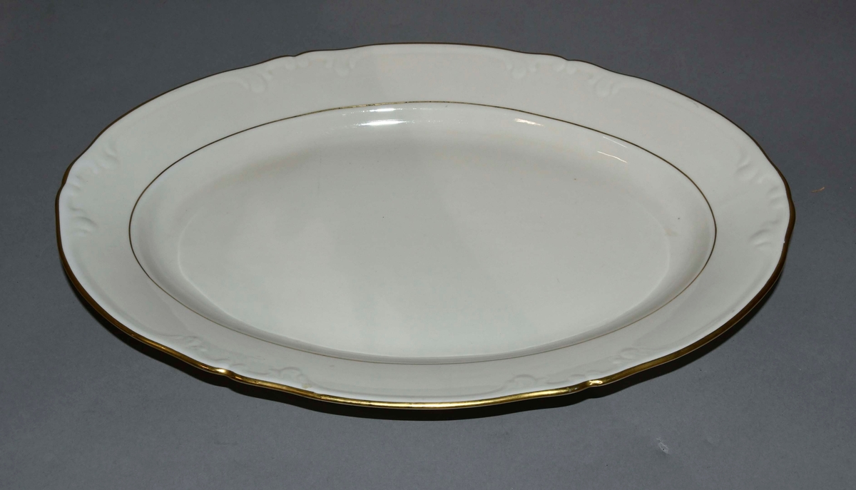 Hvitt serveringsfat av glassert keramikk, med profildekor og bølgete kant.