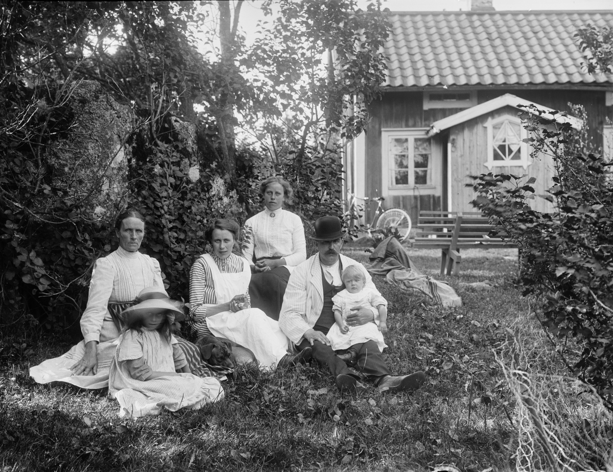 Grupporträtt - familj i trädgård framför bostadshus