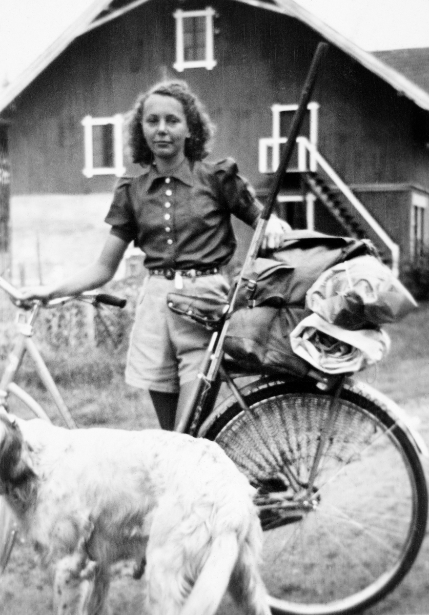 Marie Horst (seinere Marie Horst Eggen) fotografert idet hun var klar til å dra på sykkeltur fra Elverum til Rondane sommeren 1940.  Marie poserer med en damesykkel der det var bundet en ryggesekk til bagsjebrettet ved hjelp av reimer.  Marie var kledd i shorts og en kortarmet bluse.  Framfor henne ser vi en hund, og i bakgrunnen gavlen på en låvebygning.
