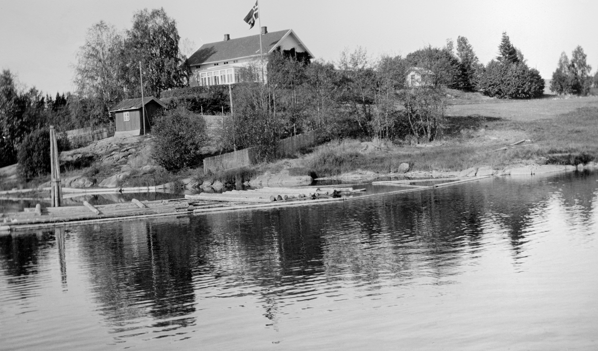 Bebyggelsen på eiendommen Lund ved Fetsund i Akershus.  Fotografiet er tatt fra Glomma, som her renner ut i nordenden av innsjøen Øyeren.  Lund lå på en bergknaus med god utsikt over elva og lenseanlegget, som ble administrert fra Lund.  Lensebestyrerne og familiene deres bodde i det kvite våningshuset sentralt i bildet.  På en bergknaus nedenfor sto det et lite hus med saltak.  På vannspeilet ser vi (til venstre) en dykdalb, en pælekonstruksjon som på Fetsund ble kalt for «gæll’je», ei lense og litt flytende tømmer.