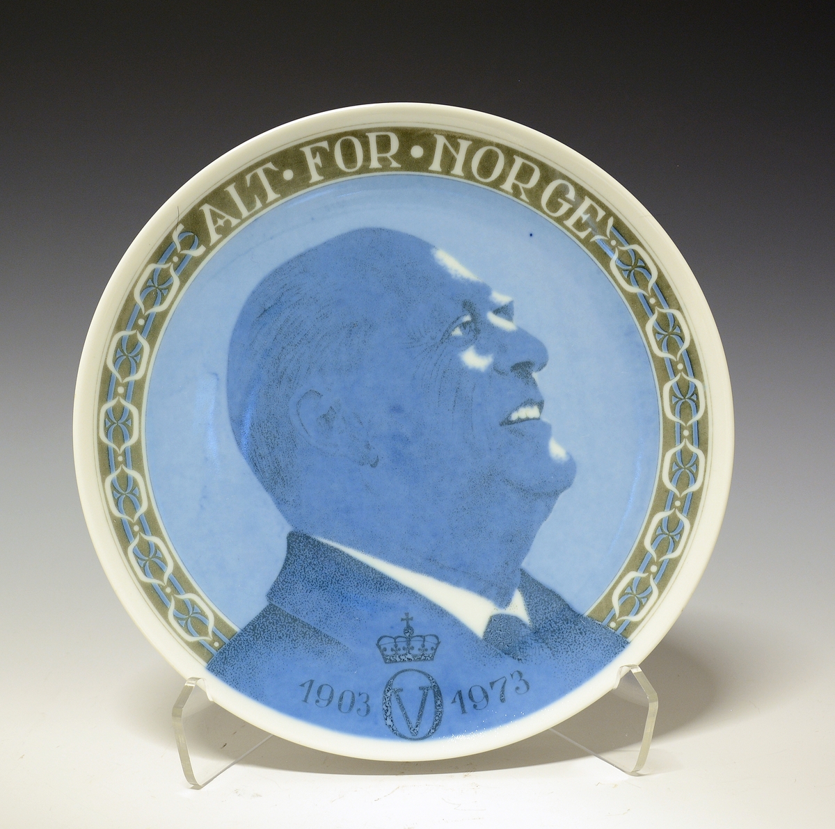 Platte med sideportrett av Kong Olav i anledning hans 70-årsdag. På fanen en hvit og blå bord på grønn bakgrunn på hver side av kongen.