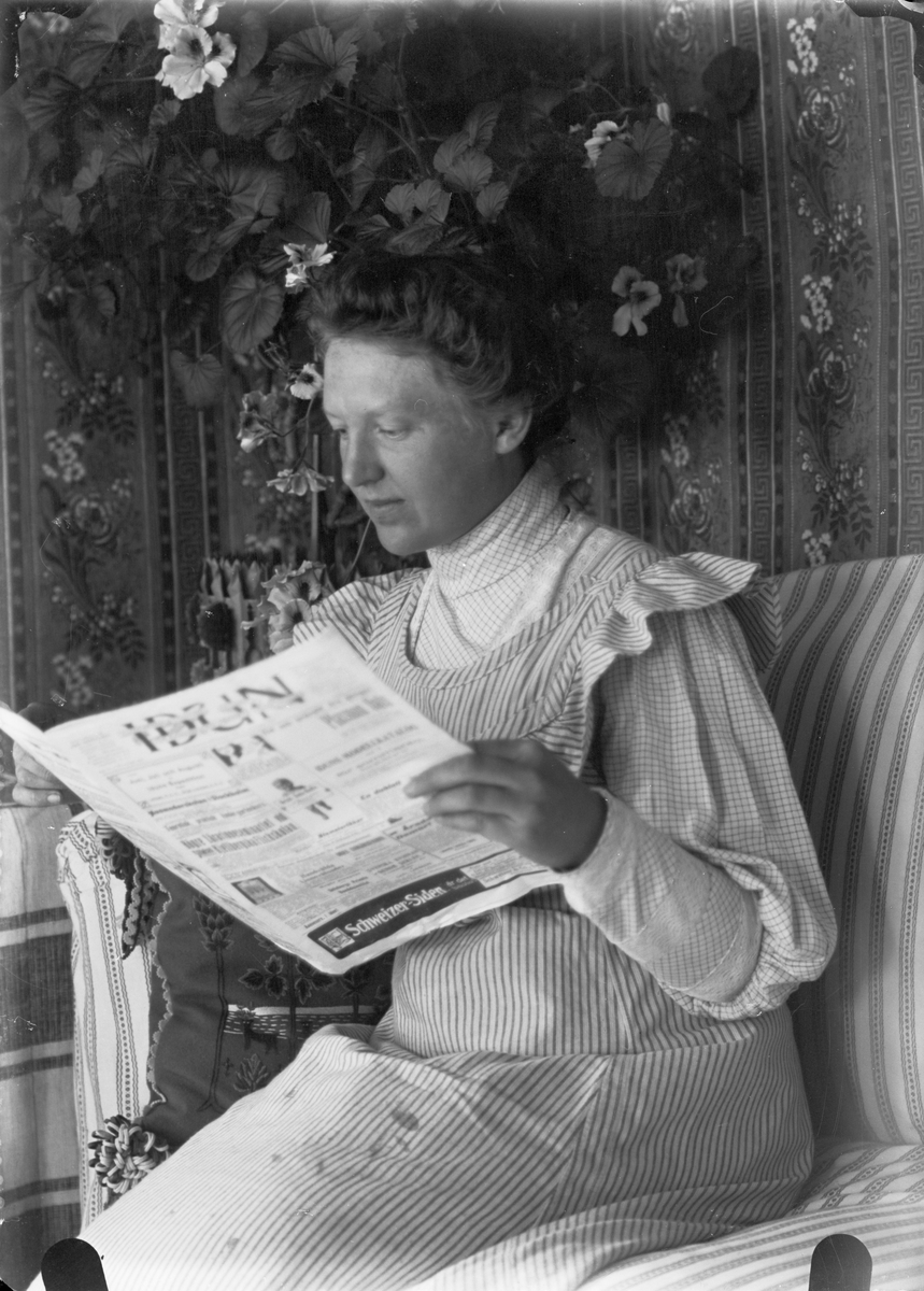 Anna Alinder sitter i soffan och läser tidningen Idun, Sävasta, Altuna socken, Uppland
