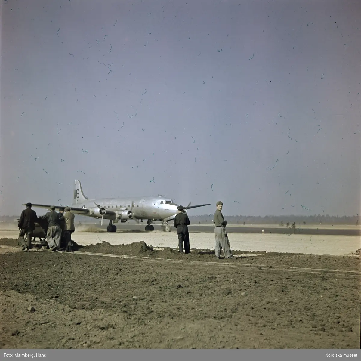 Berlinblockaden. En grupp arbetare på ett flygfält. I bakgrunden ett amerikanskt transportflygplan av typen Douglas C-54 Skymaster.