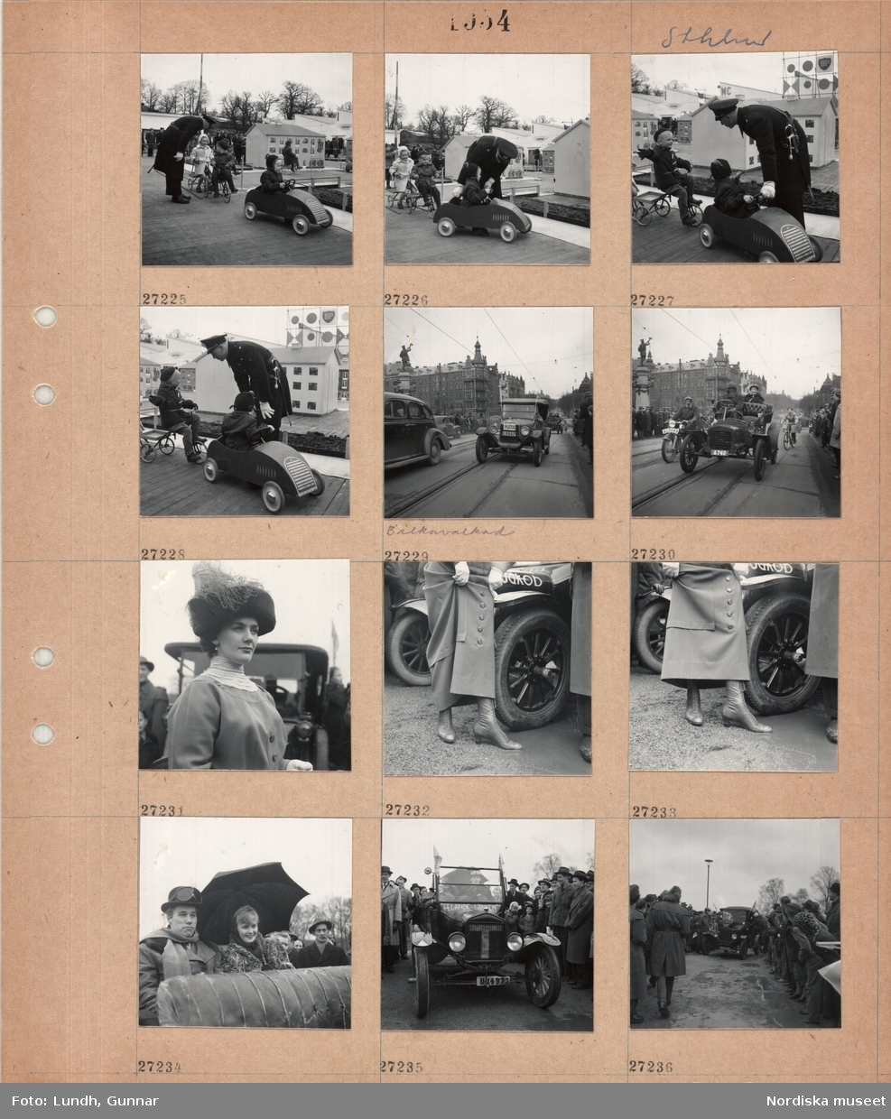 Motiv: Sthlm (Stockholm) ;
En man i uniform dirigerar barn i trampbilar och på trehjulingar som åker i en ministad med trafikmärken för att lära sig trafikregler, historiska bilar och kvinnor och män i historiska kläder åker förbi människor som står på trottoaren "Bilkavalkad", en kvinna i historiska kläder.