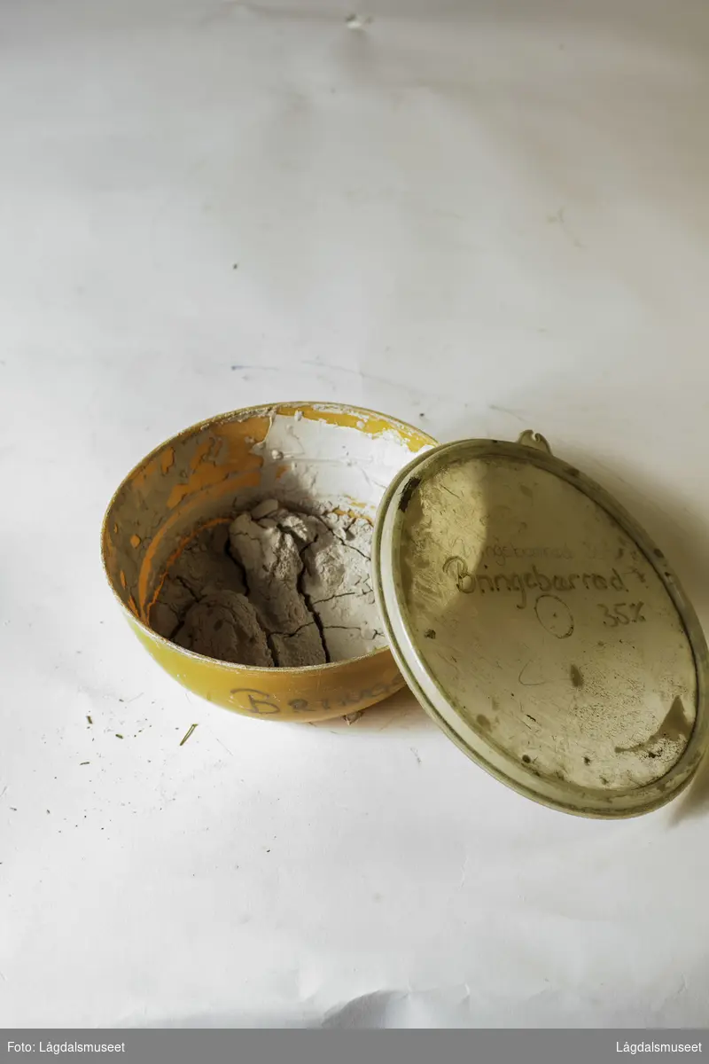 Plastbolle med lokk med uttørket pipeleire i fargen bringebærrødt. Pipeleiren ble brukt til begitting av keramikken.