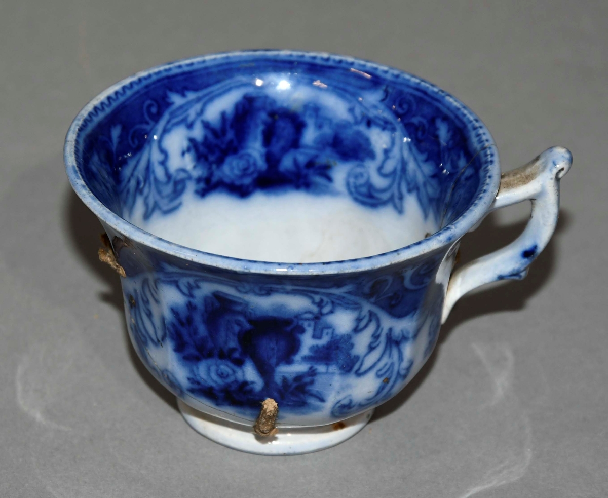 Kopp av glassert keramikk. Hvit grunnfarge, med blå dekormaling.