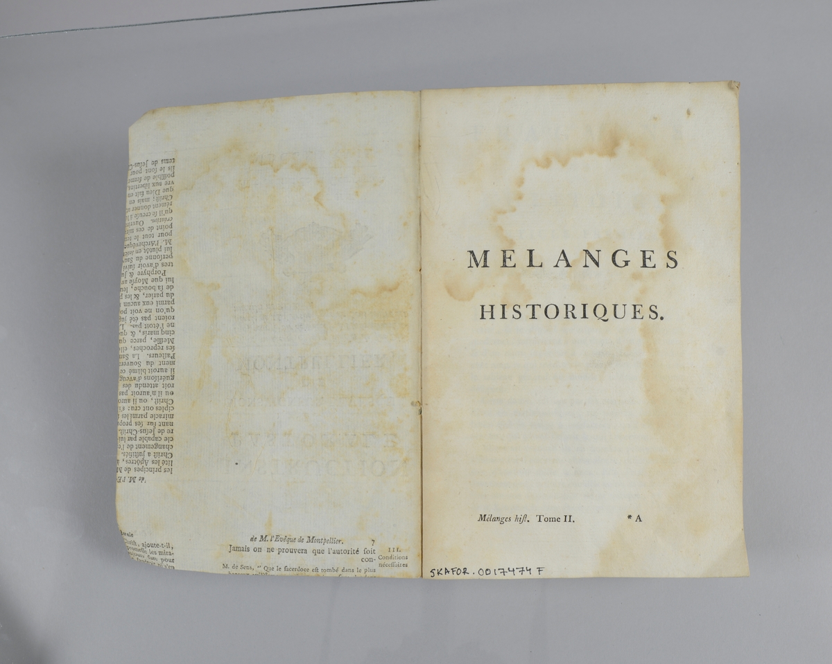 Bok, pappband,"Oeuvres completes de Voltaire", del 28 "Melanges historiques", tryckt 1785.
Pärmen klädd med gråblått papper, på pärmarnas insidor klistrade sior ur annan bok. Med skurna snitt. På ryggen klistrad pappersetikett med tryckt text samt volymens nummer. Ryggen blekt.
