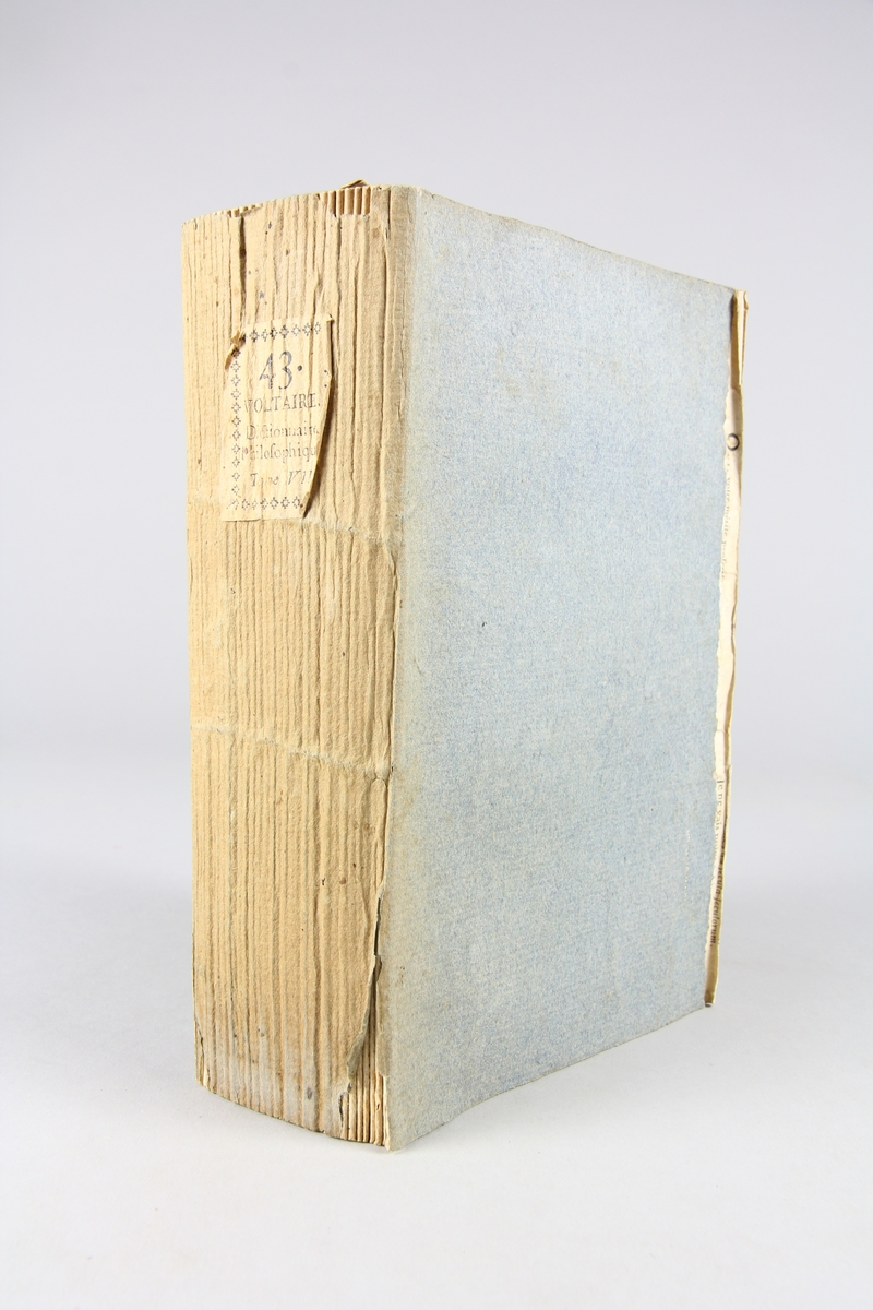 Bok, pappband,"Oeuvres complètes de Voltaire." del 43, tryckt 1785.
Pärm av gråblått papper, på pärmens insidor klistrade sidor ur annan bok. Med skurna snitt. På ryggen pappersetikett med tryckt text med volymens namn och nummer. Ryggen blekt.