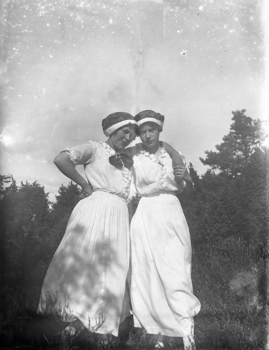 Systrarna Dagny och Alice Gustafsson i vita sommarklänningar håller om varandra.