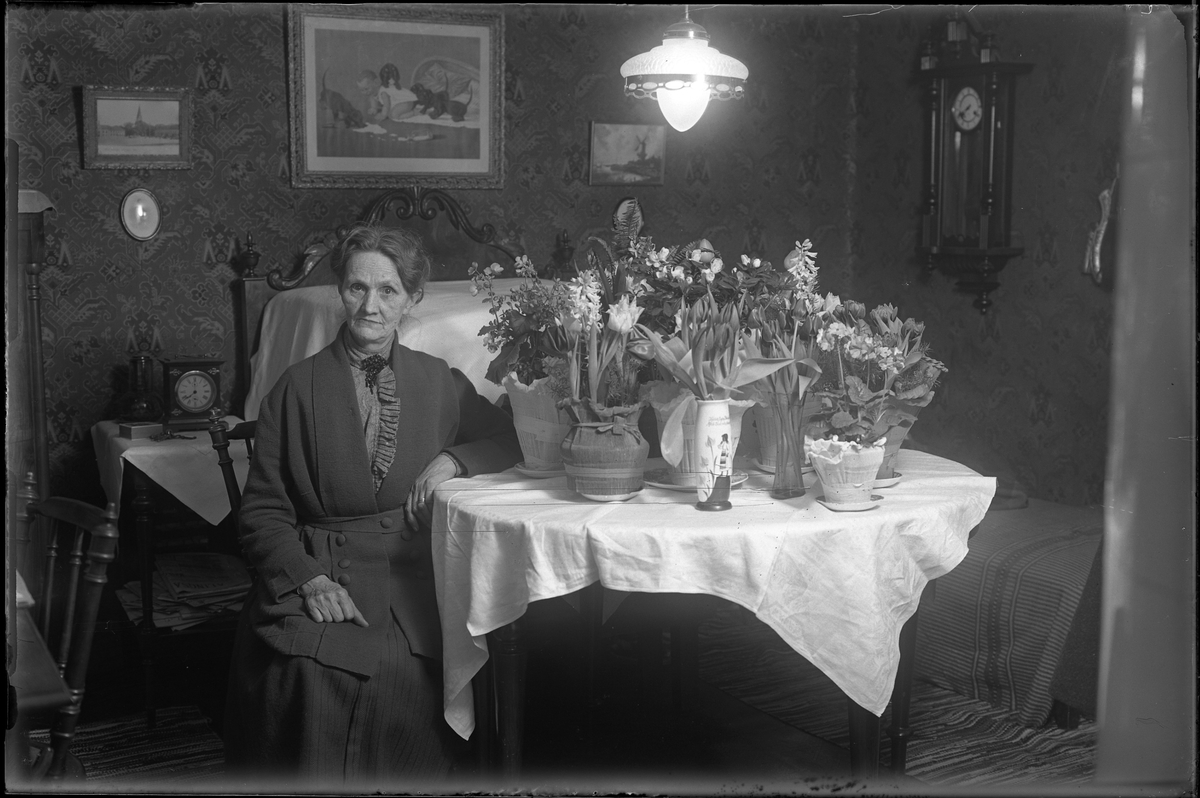 Porträtt av Fru Nordgren, förmodligen i samband med en jämn födelsedag med tanke på blommorna på bordet bredvid henne.
