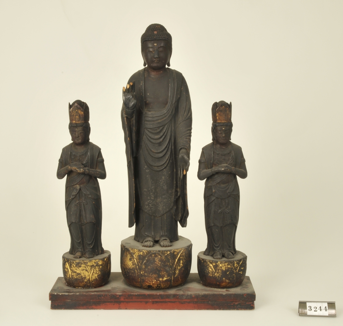 Budda omgiven av två bodhisattvas.
Tre personer - en större och två mindre sammonterade.
Svartmålade och förgyllda.
Höjd: 290 resp 450 mm.


Adelsköldska samlingarna.
