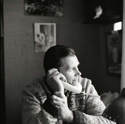 Hilding Mickelsson sitter vid ett bord och pratar i telefon med luren hållen mot ena örat, 1969.