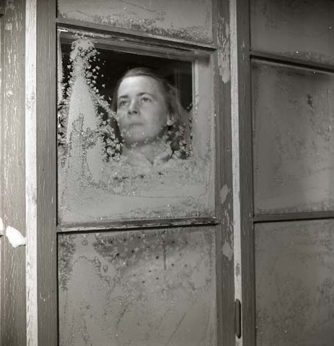 En kvinna tittar ut genom ett fönster delvis täckt av frost, 1950.