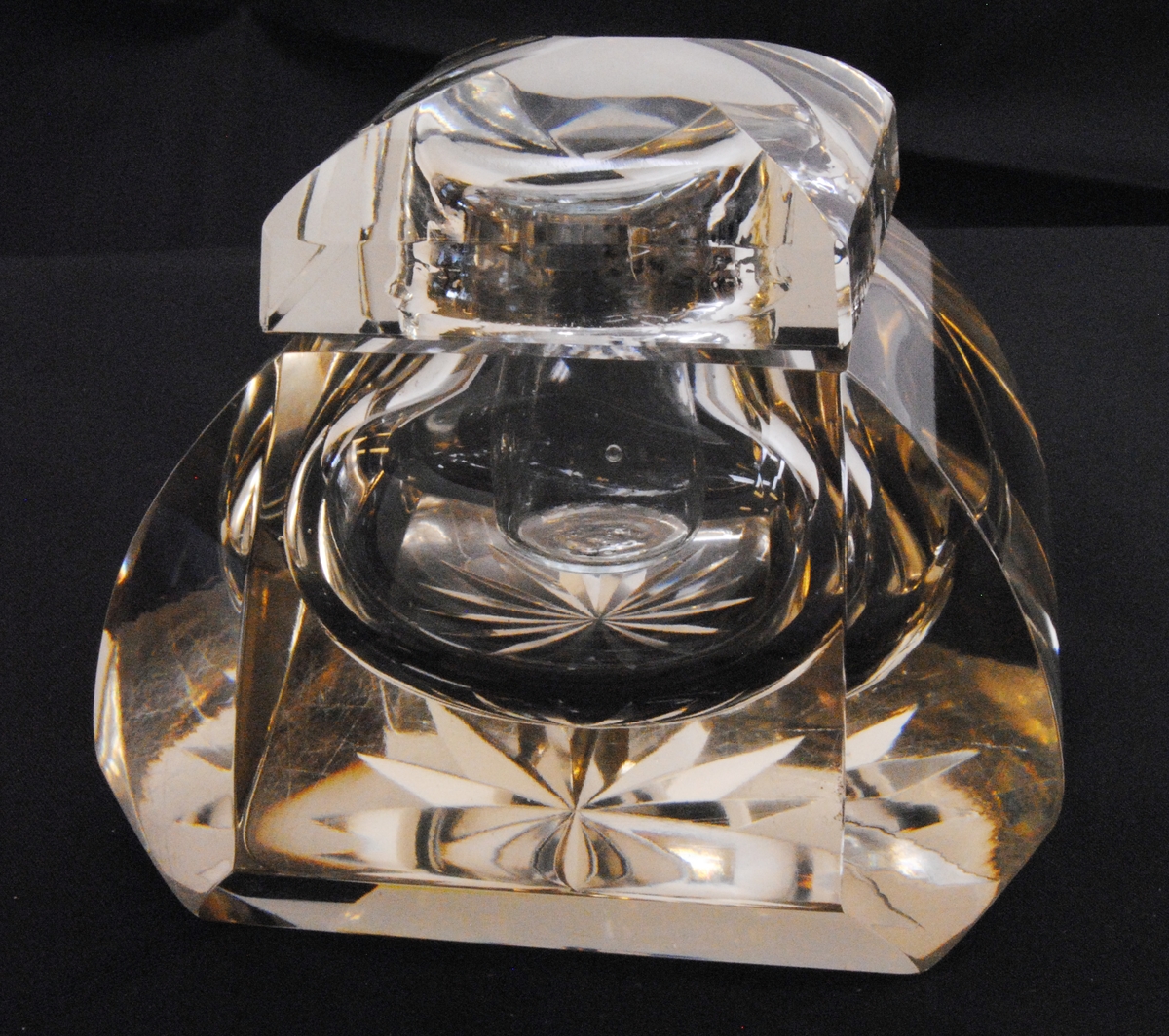 Bläckhorn av fasettslipat glas med glasinsats för bläck, samt med lock. Glasets färg har en ton av gul. Bläckhornets botten är stjärnslipad.