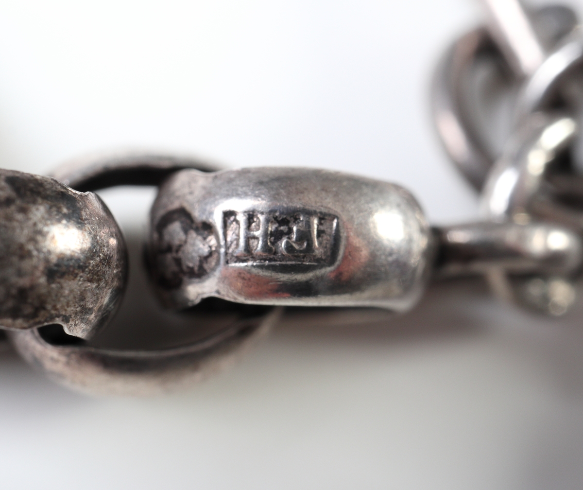 Urkedja av silver.
Genombruten kedja med tillhörande urnyckel och hake. En extra nyckel i mässing och stål medföljer.
Inskrivet i huvudkatalog 2018.