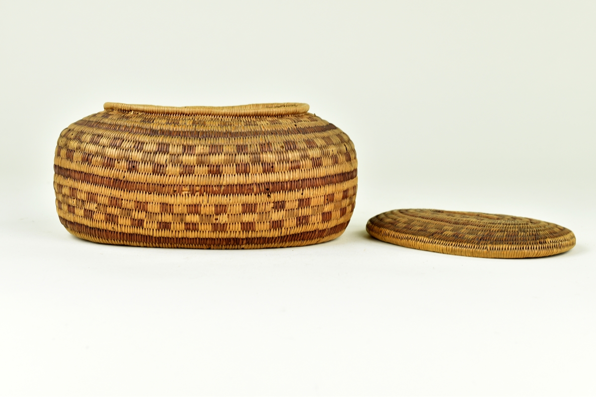 Flätad oval ask med lock. Vide i två toner har använts för att mönstra asken i ränder och rutor.