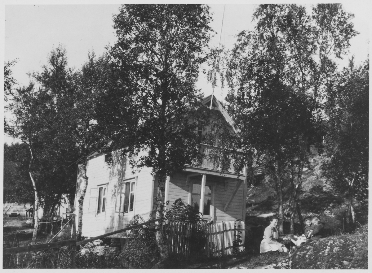 Hus eller hytte i Kanebogen. Kvinne med hund og to barn i forgrunnen til høyre.