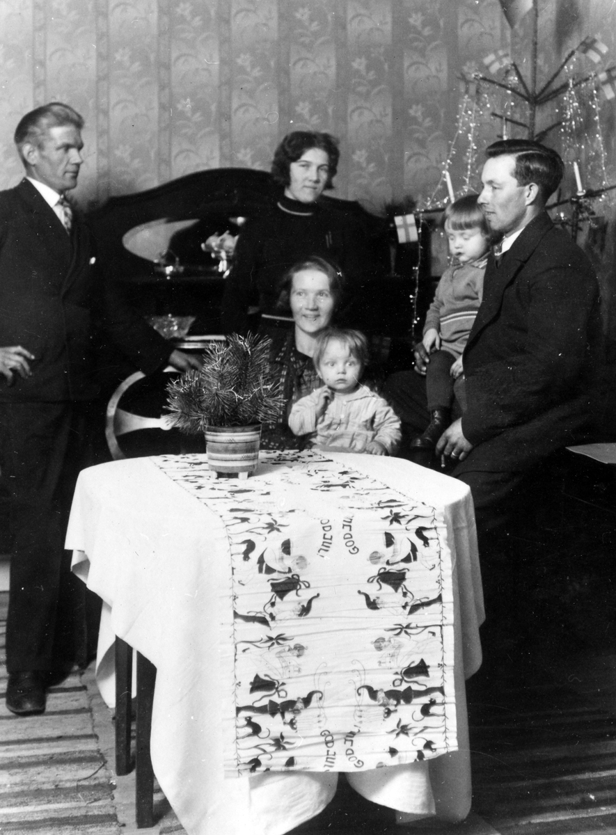 En familj har samlat kring ett bord vid juletid. Kvinnan som sitter heter Dagmar och barnet hon håller heter Stina. Stina Gifte Sig sedan med Harry Lycke.