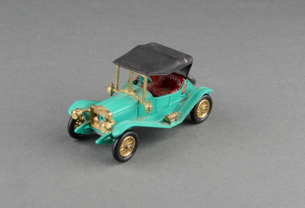 Modell av veteranbil 1911 Maxwell roadster med kalesje og enkelt sett seter.  Lave hjul og reservehjul bak. I originaleske (som en fyrstikkeske i forstørret format).