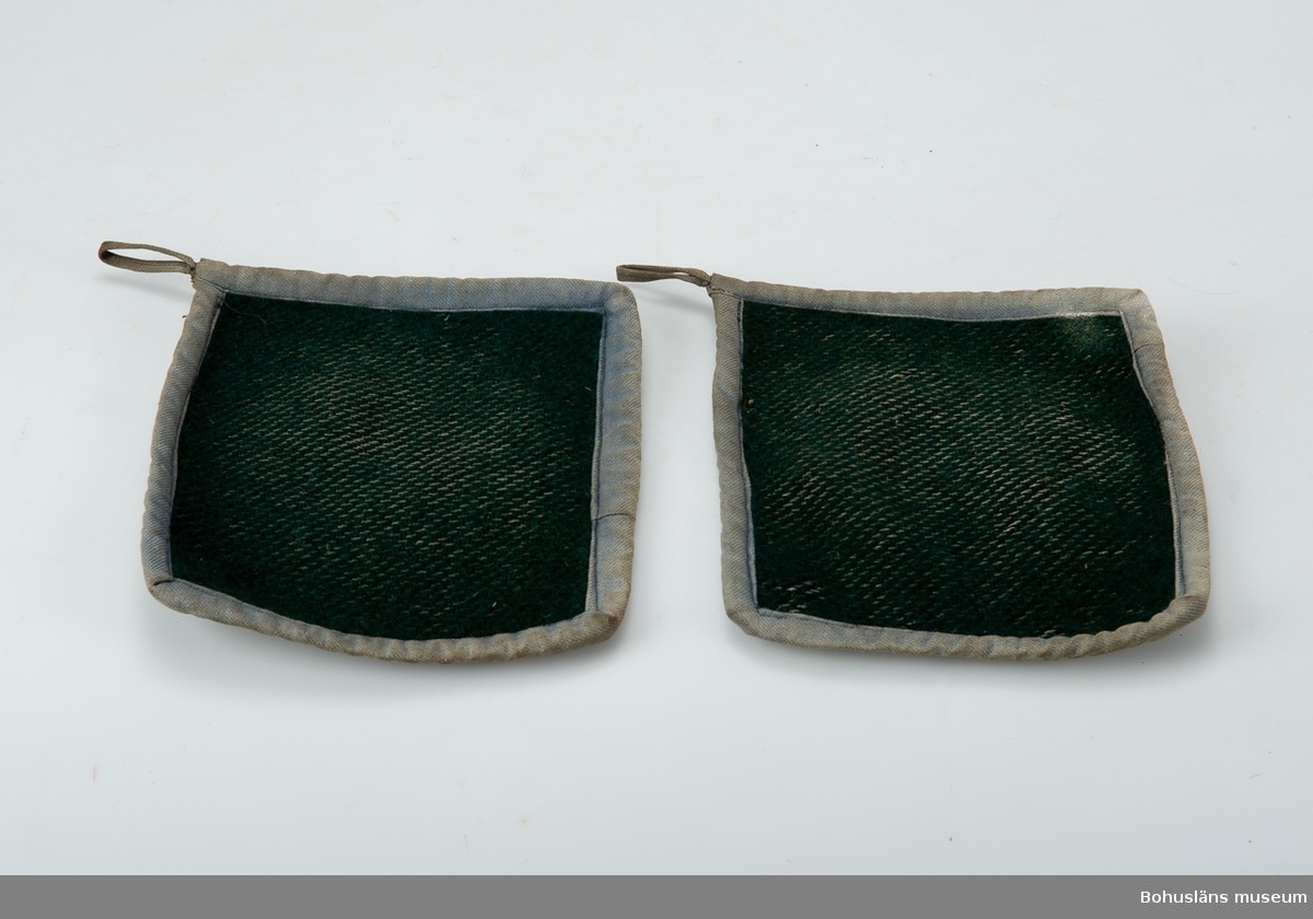 Ett par slitna grytlappar av kypertvävt ylletyg kantade med bomullsband.
Möjligen tillverkade av äldre ytterplagg.