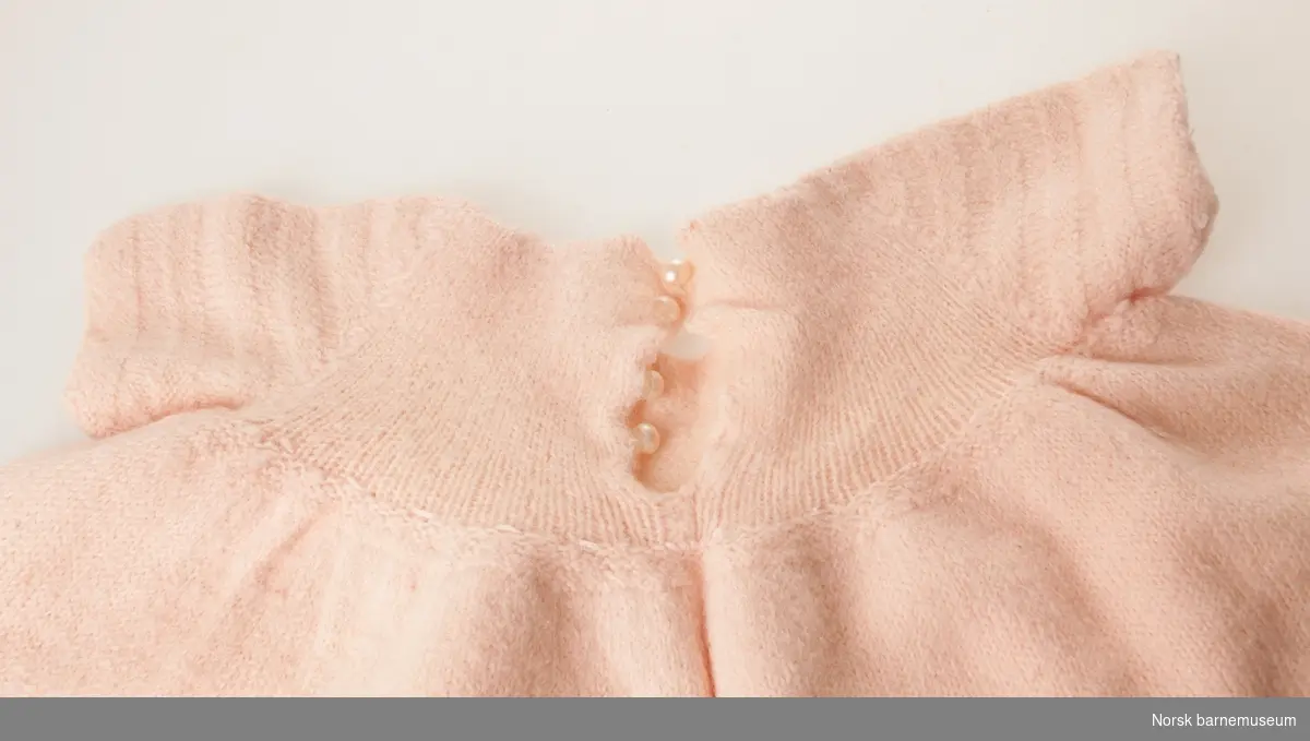 Rosa kortermet strikkekjole til barn, med perleknapper bak.