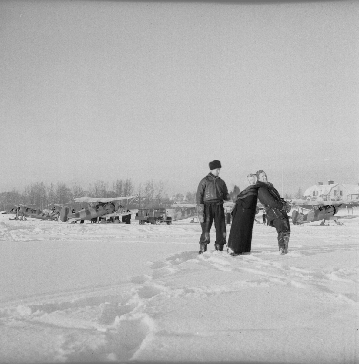 Flygförarna Arne Frykholm samt Åke "Sammy" Nettelbladt-Hollsten samt en kvinna vid namn Maj-Britt står på flygfältet på Kyrksjöns is i Ljusdal den 1 januari 1940. I bakgrunden står sex stycken flygplan Gloster Gladiator. Flygplanen flög senare vidare till Svenska frivilligkåren i Finland, F 19.