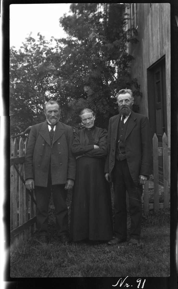 Portrett av tre personer, tatt foran et hagegjerde.