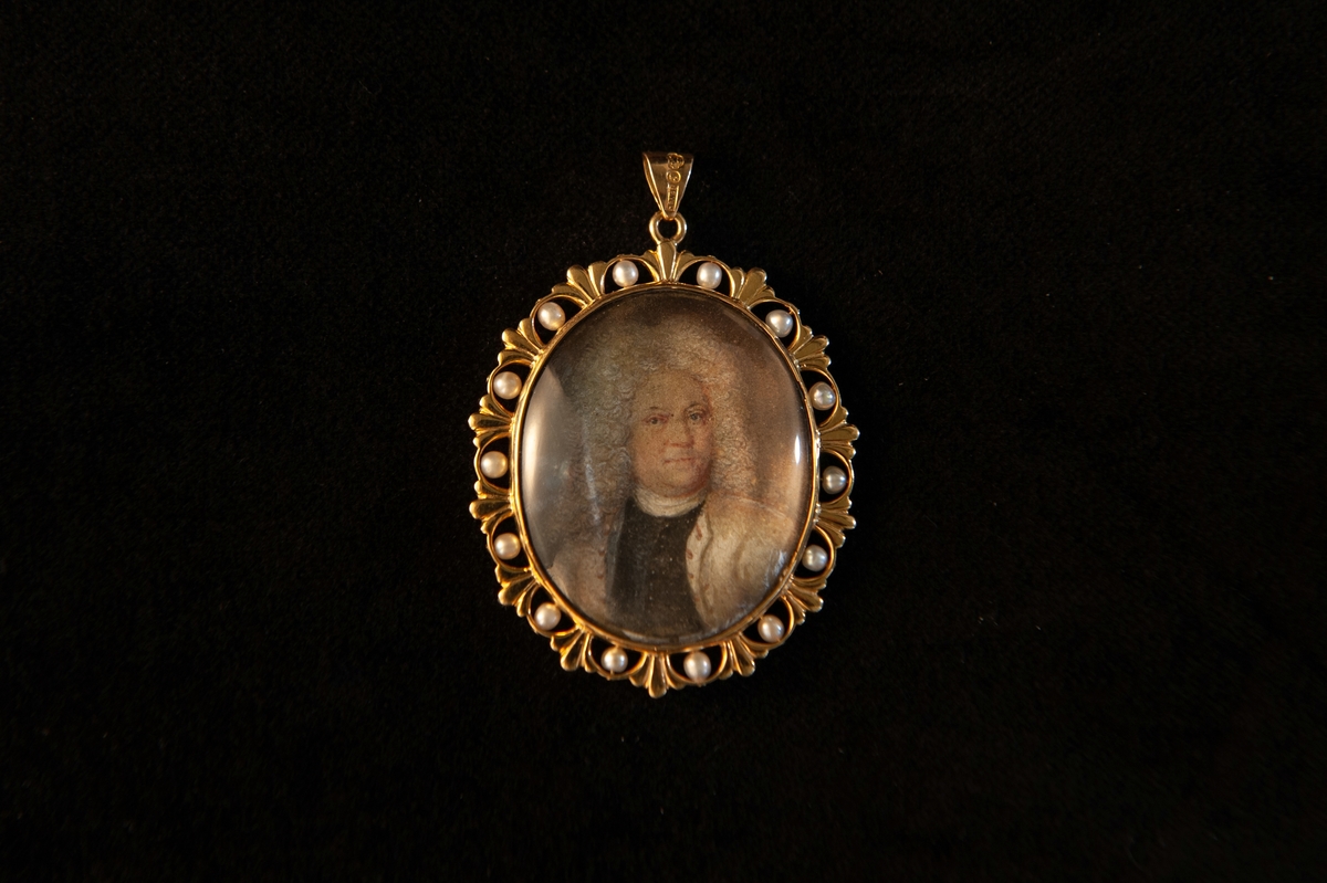 En oval medaljong med målat porträtt (på elfenben) av äldre herre i grå allongeperuk (bröstbild). Senare infattning och ram av guld, delvis genombruten, med infattade pärlor. Miniatyr.