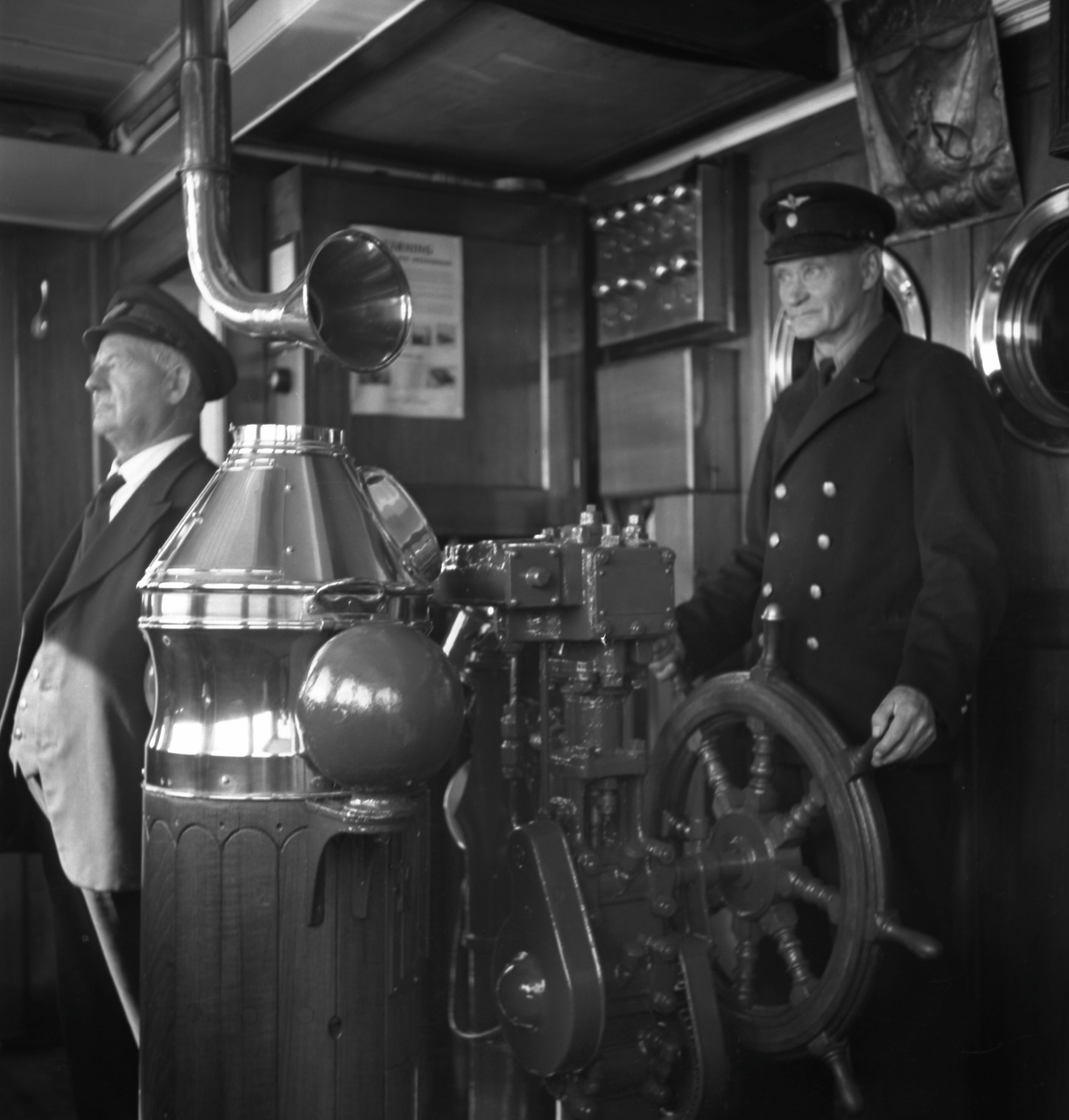 Styrman Karl Nilsson och rorgängare Anton Nilsson i styrhytten på  tågfärjan Drottning Victoria. Trafikerade linjen Trelleborg - Sassnitz.  Inkallades som hjälpkryssare (hjkr 3) under andra världskriget. Fotot möjligtvis taget under kriget.