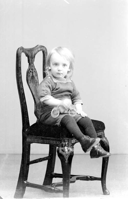 Åke Larsson-Ölmeskog, en liten pojk sittande på en stol med en leksabil eller cykel i handen.